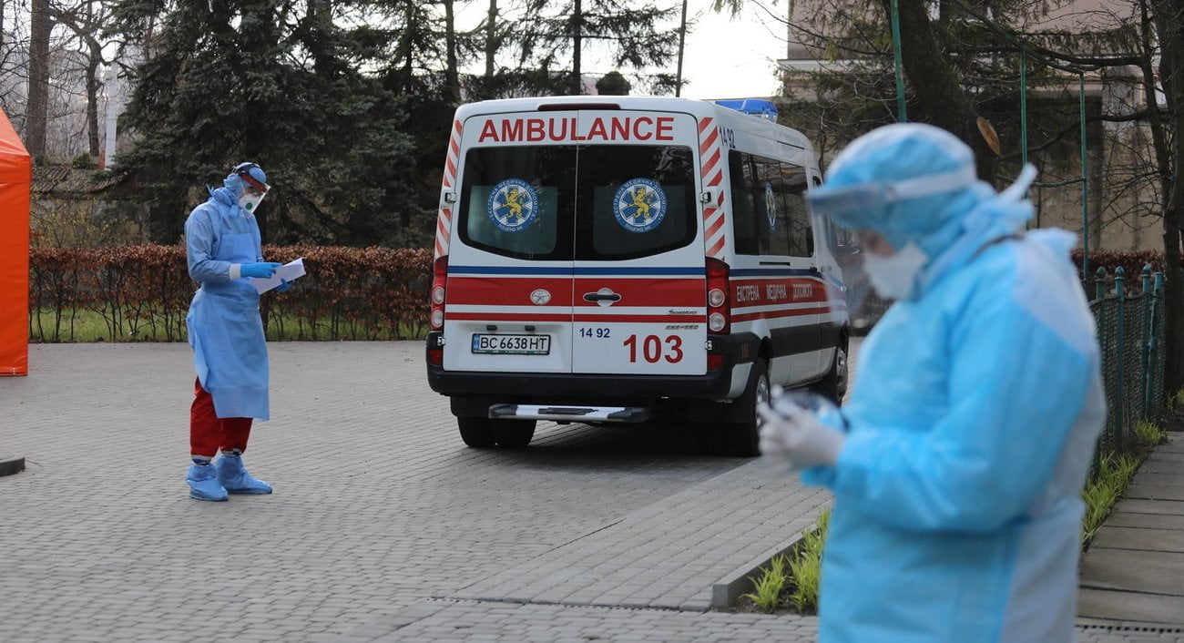 A medical professional in Ukraine holding a clipboard with data charts against a blurred hospital background.