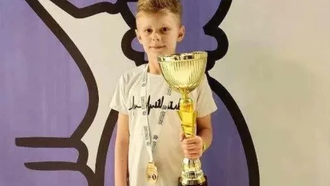 Ukrainian 10‑year‑old chess champion holding trophy after defeating a neutral Russian opponent at the U10 World Rapid Chess Championship.