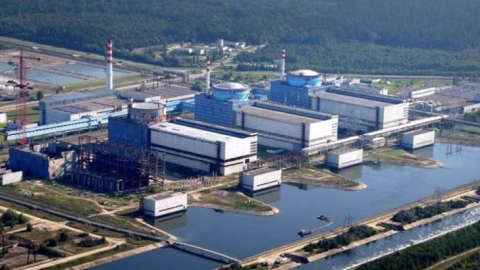 Energoatom nuclear plant construction site with cranes and Zelenskyy press backdrop, showing energy expansion under political and corruption scrutiny.