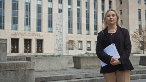 Kelsie Kimberlin holding lawsuit documents on the steps of the United States District Court for the District of Columbia in Washington.