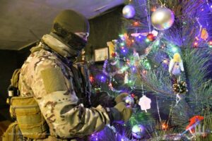 Ukrainian defender in uniform stands by a Christmas tree, celebrating New Year during wartime resilience and hope.
