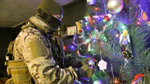Ukrainian defender in uniform stands by a Christmas tree, celebrating New Year during wartime resilience and hope.