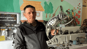 Ukrainian veteran creating techno art sculpture from scrap metal in workshop showing welding tools and recycled materials